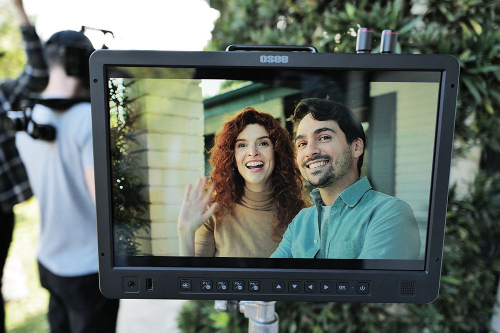 A smiling couple seen on a film monitor during a TV or movie production shoot outdoors.