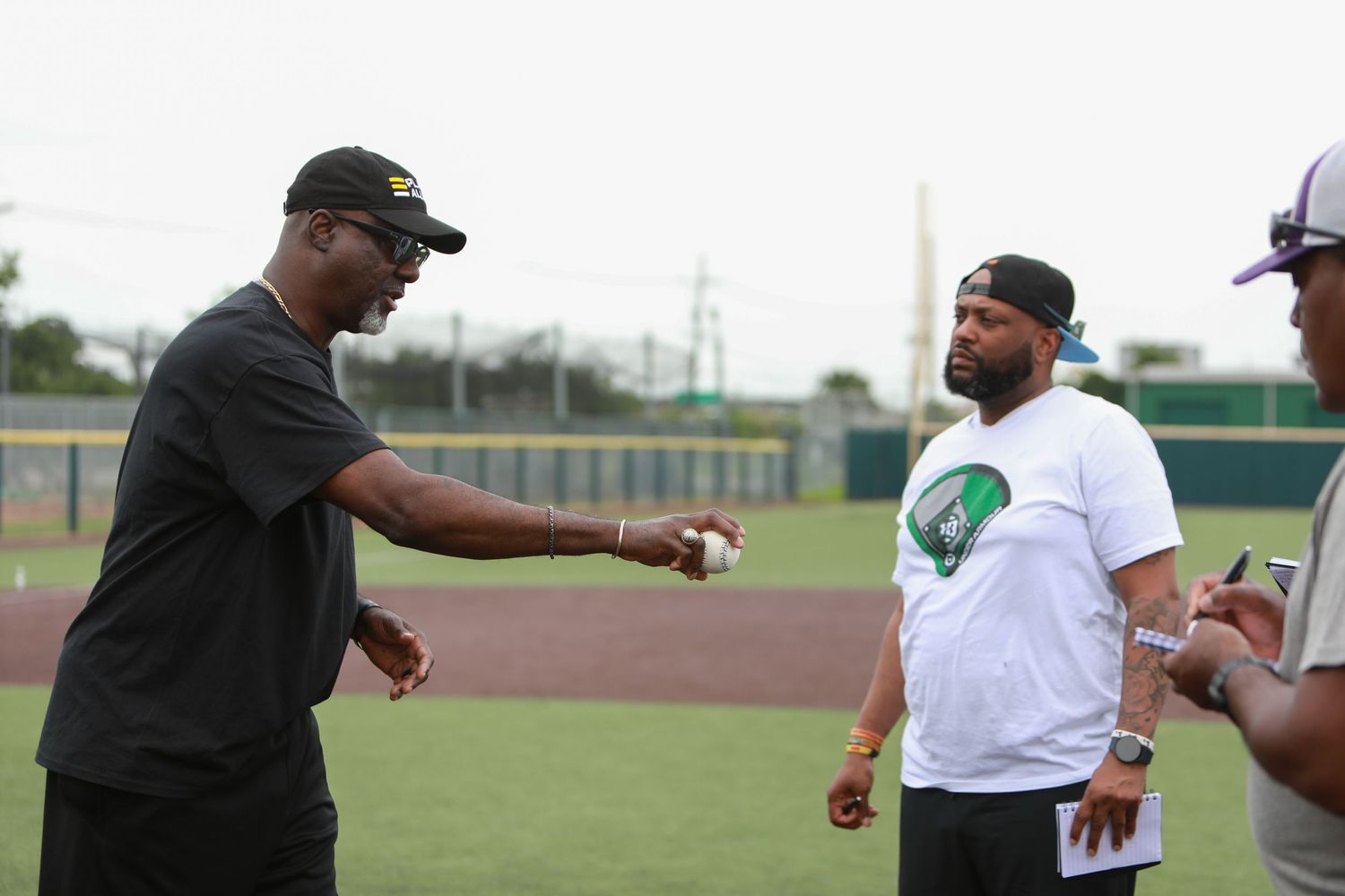 Baseball players interact during practice on a baseball diamond field.