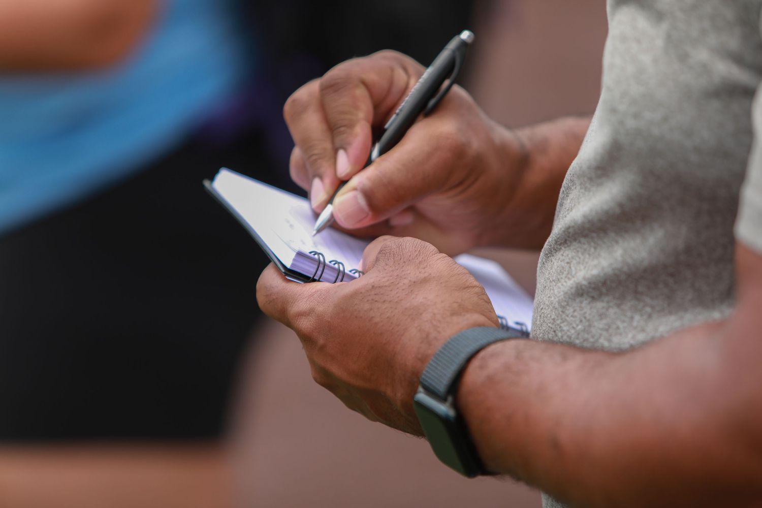 Close up of hands writing on a notepad while wearing a fitness tracker.