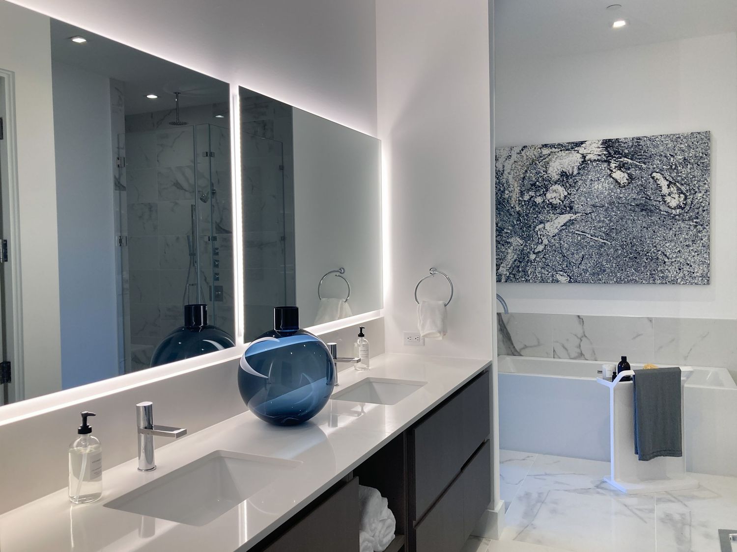Modern white bathroom with double vanity, large mirror, and contemporary artwork.