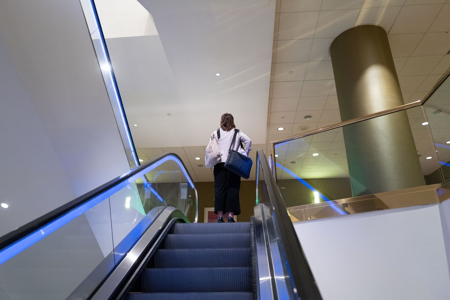 Person ascending illuminated escalator in modern building interior.