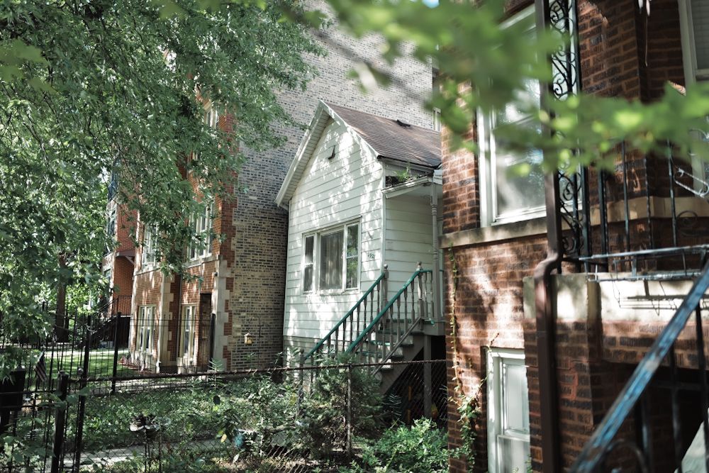 Charming brick and white siding residential homes with exterior staircases surrounded by lush trees.