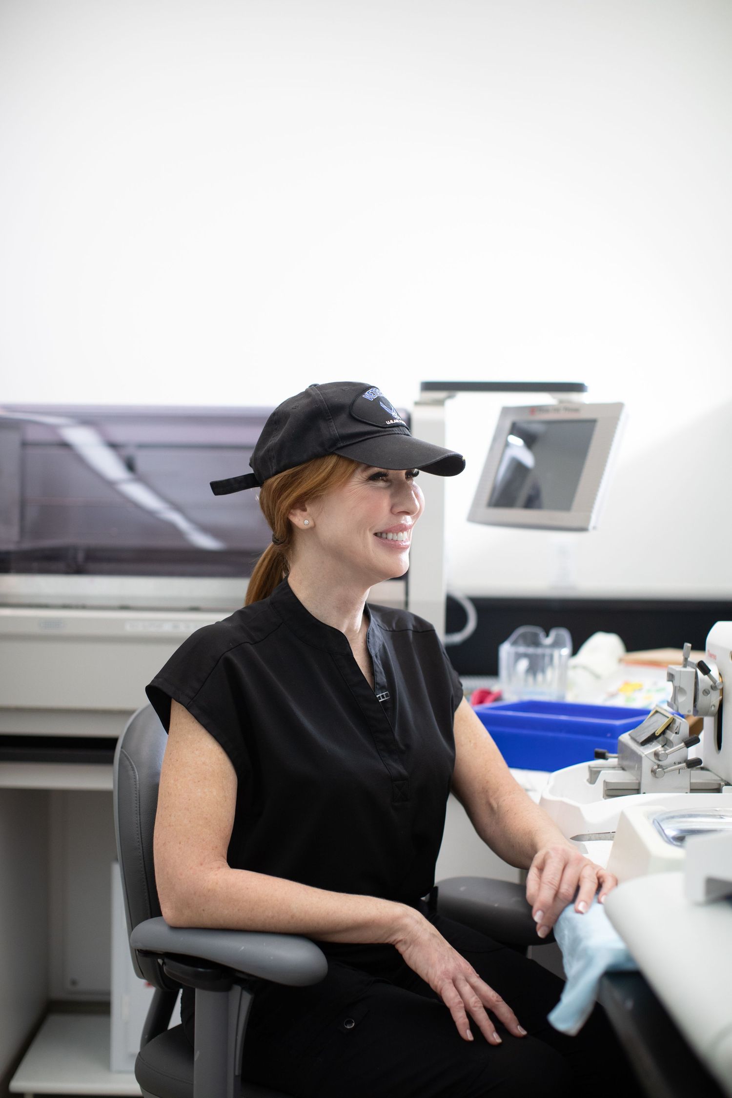 Healthcare worker in black uniform and cap working at laboratory testing station.
