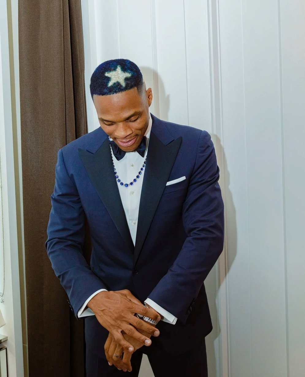 Professional athlete in navy suit and baseball cap bows head in prayer before a game.