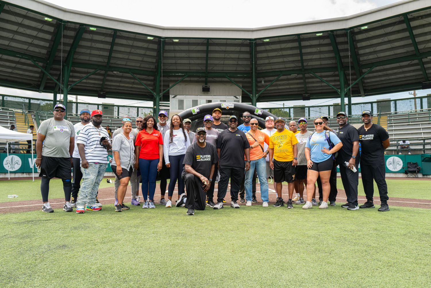 Group photo of baseball training participants and coaches on field at sports facility.