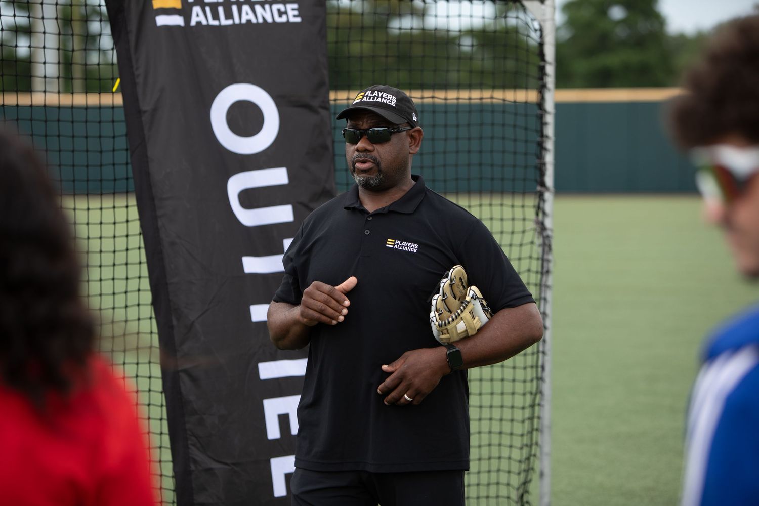 Baseball instructor demonstrating techniques next to Players Alliance banner.