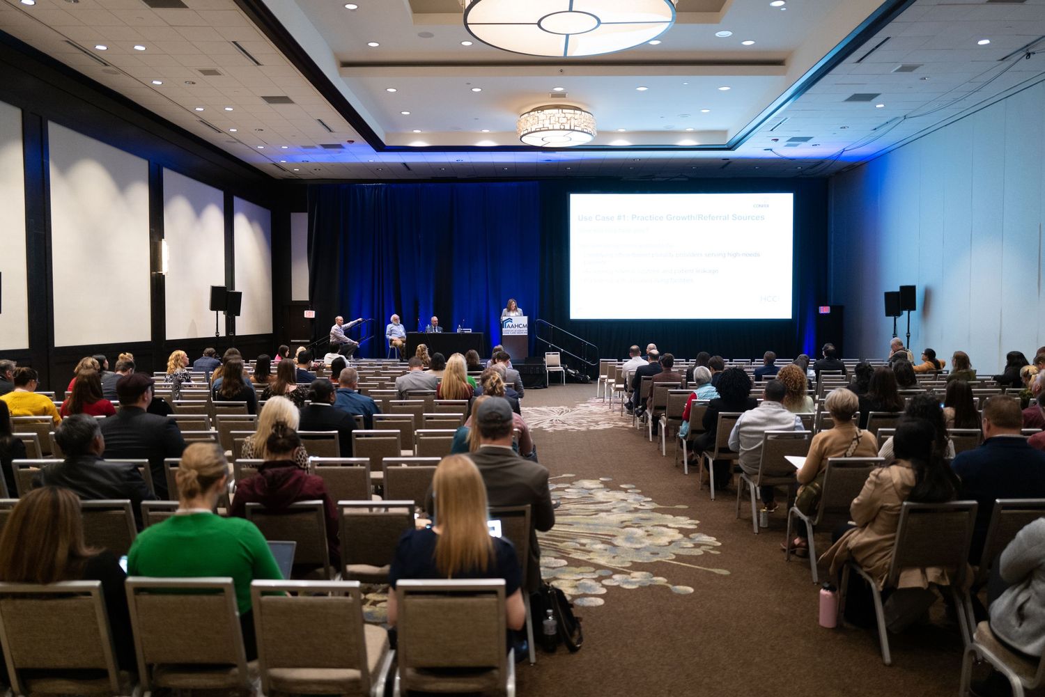 Conference presentation room with audience seated in rows facing projection screen.