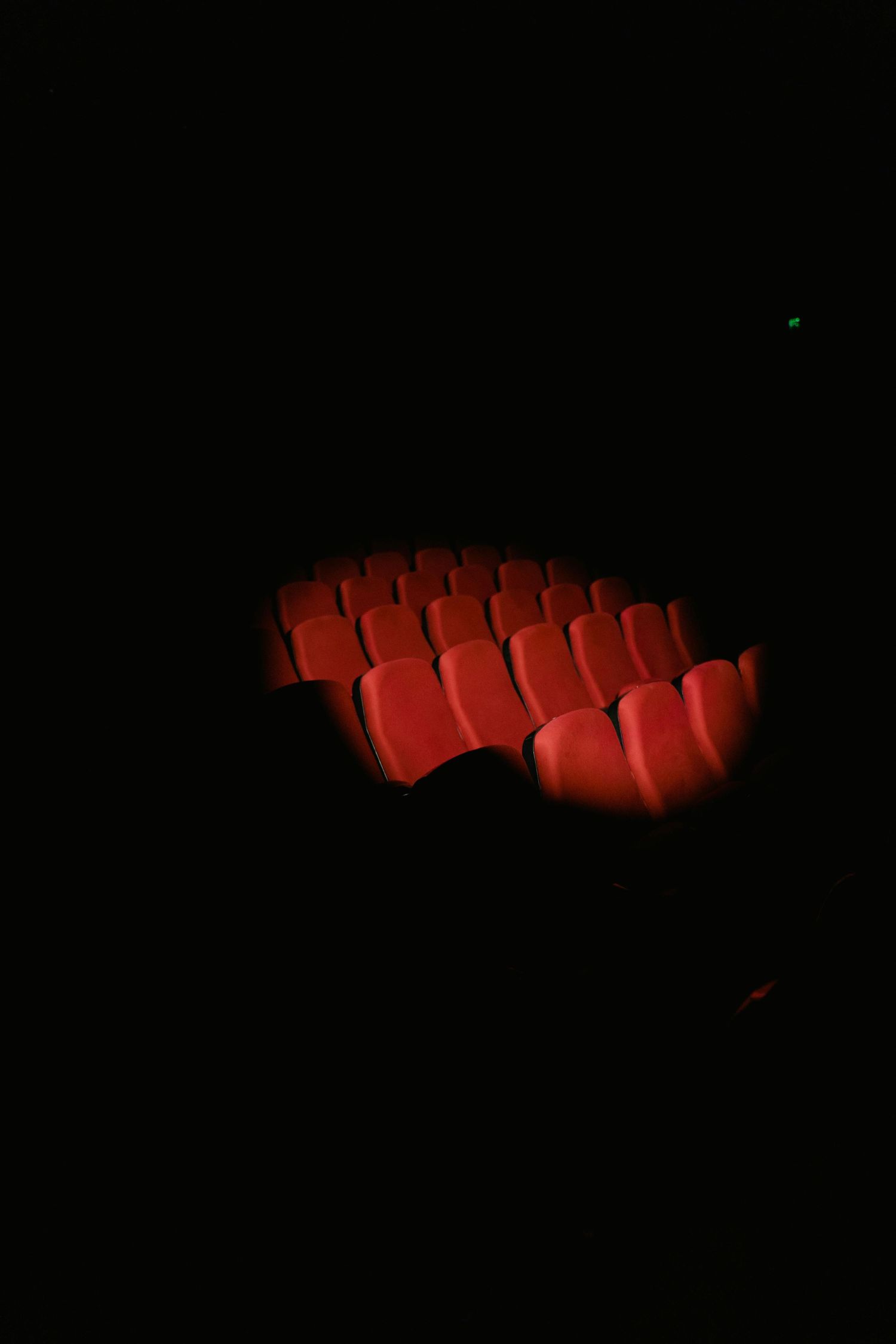 Red theater seats illuminated in darkness showing empty cinema auditorium.