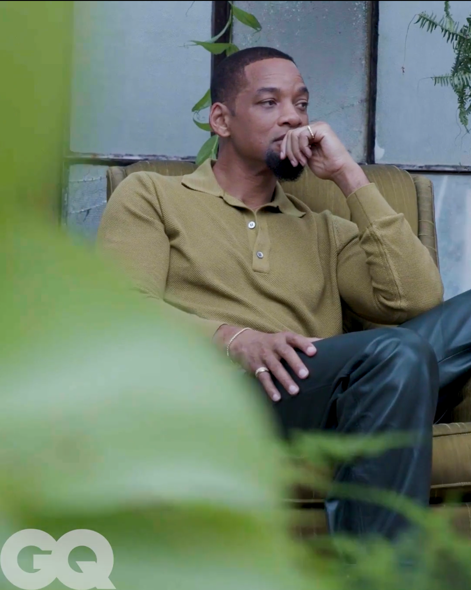 Man in olive green polo shirt sitting pensively on a chair, featured in GQ magazine editorial shoot.