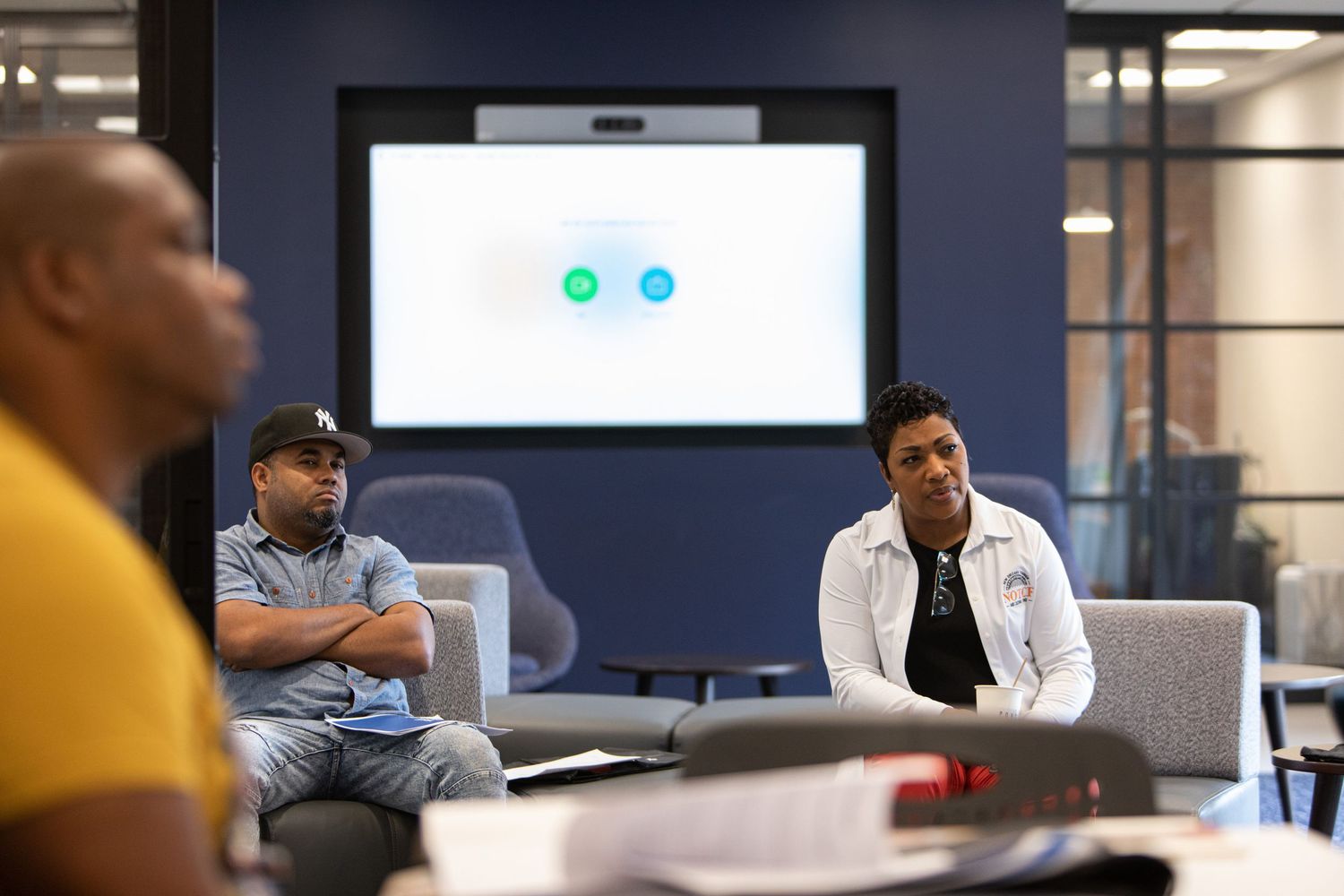 Attendees participate in a discussion during a corporate meeting with a display screen visible.