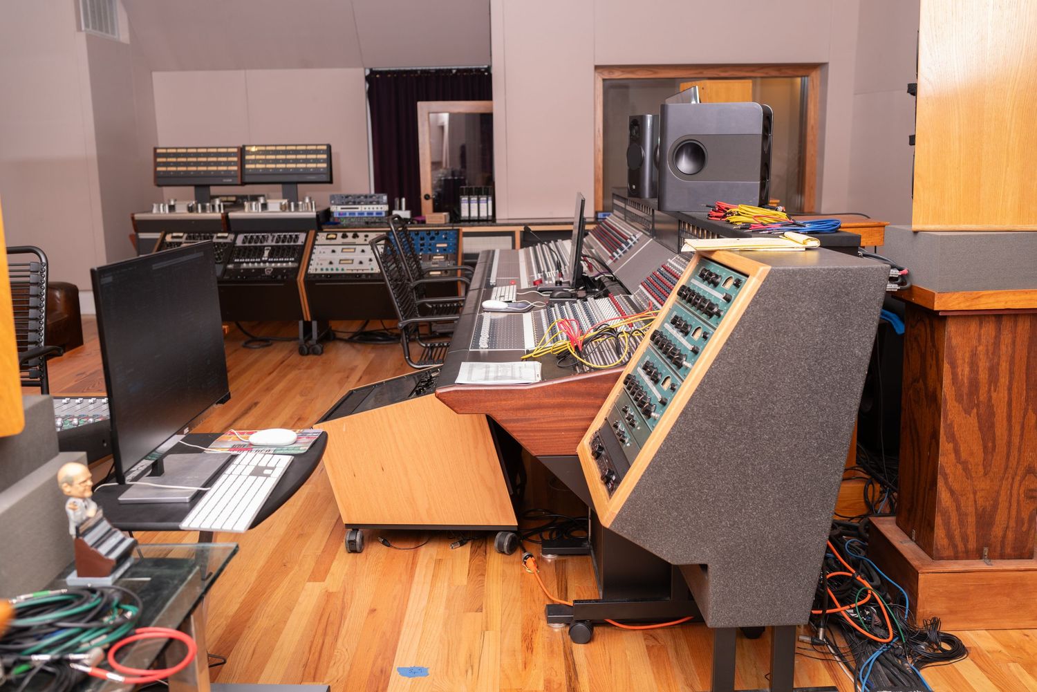 Recording studio mixing console setup with wooden floors and multiple audio control surfaces.