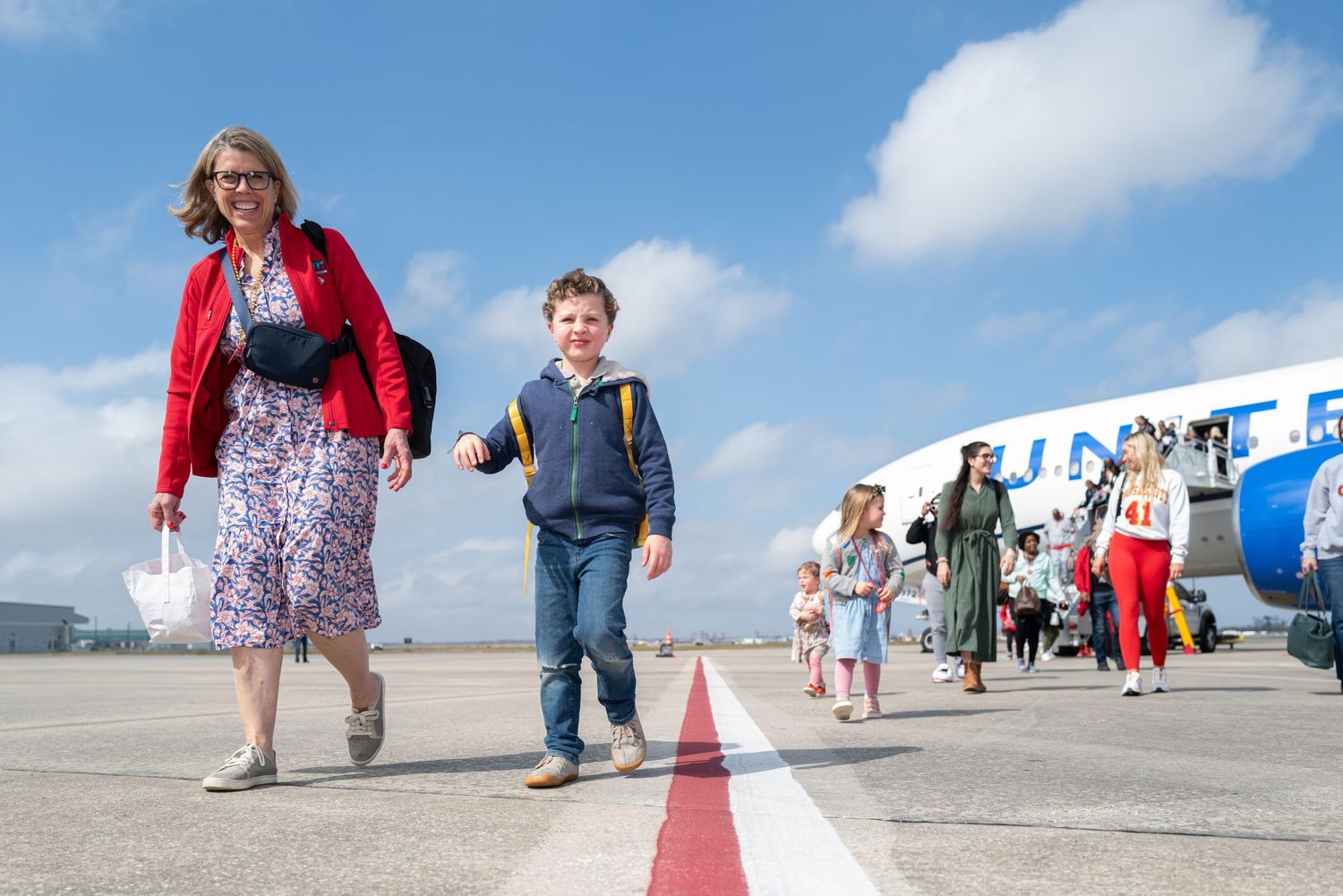 People walking along a red line on airport tarmac next to parked aircraft.