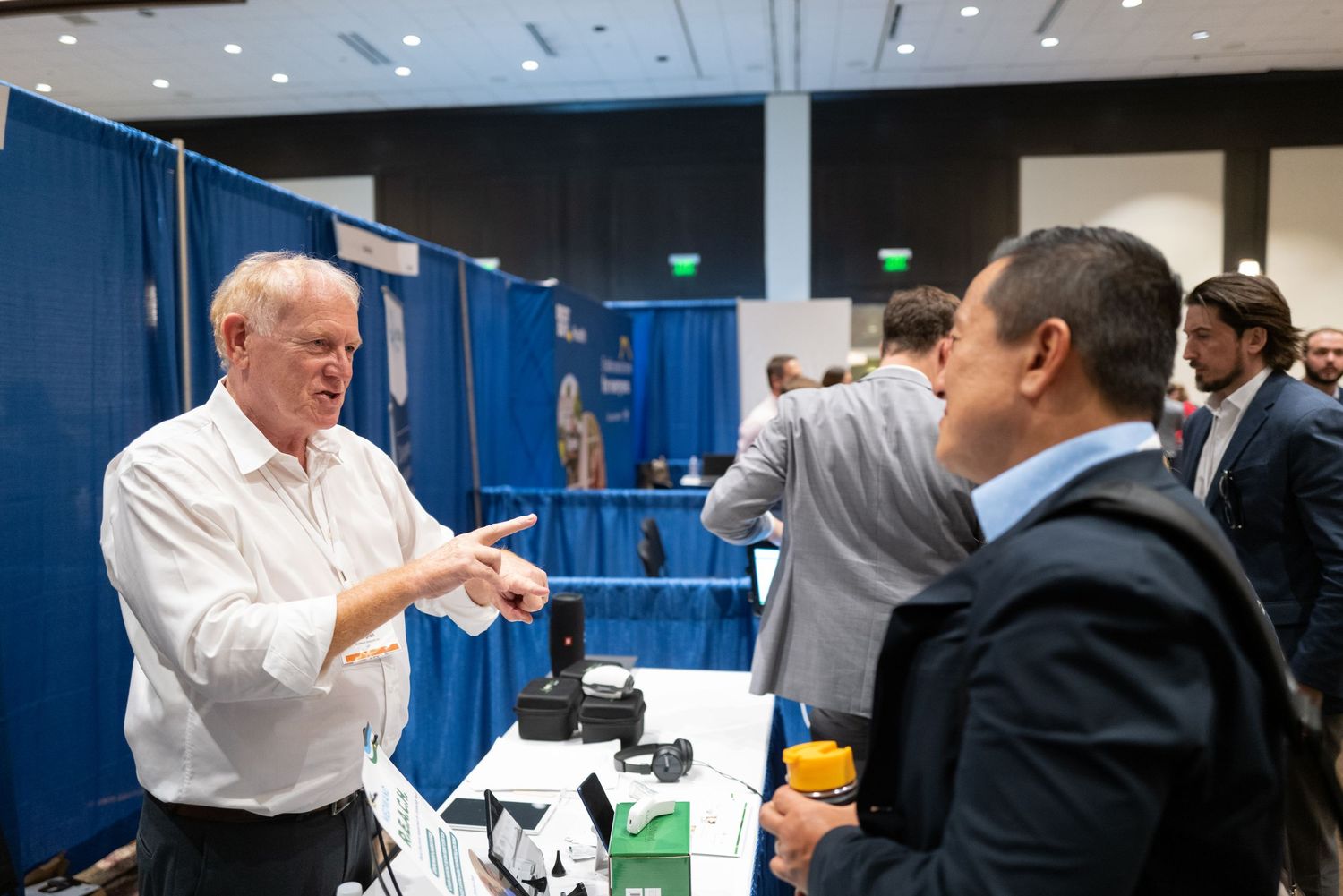 Professional networking event with exhibitors and attendees interacting at trade show booth.