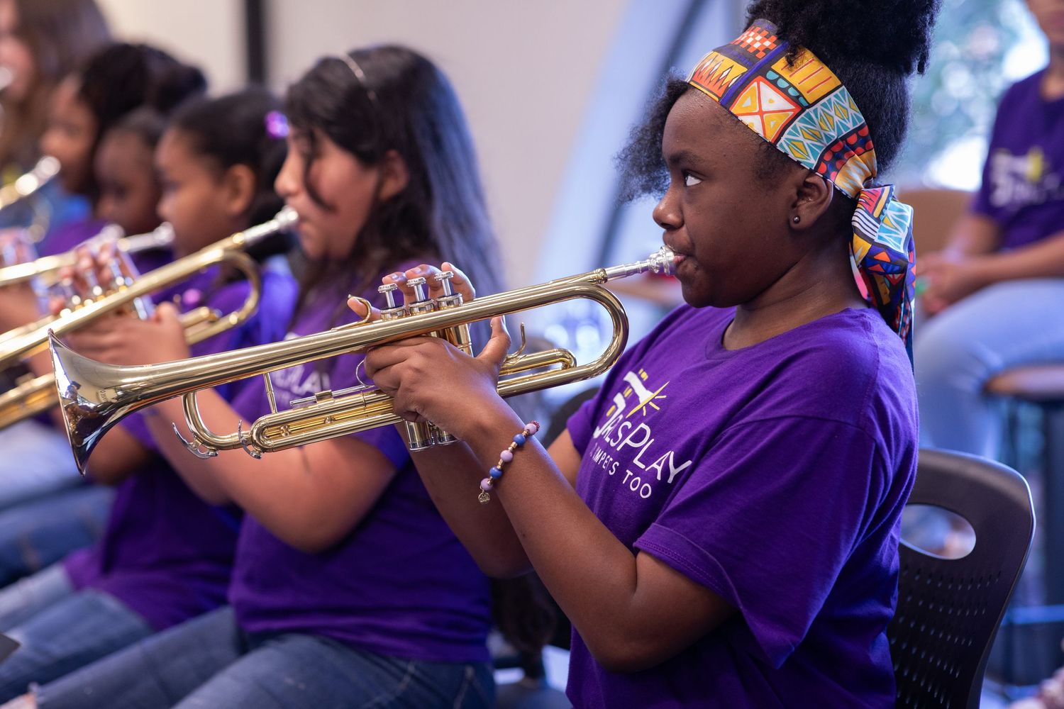 Student plays trumpet while wearing purple uniform in orchestra.