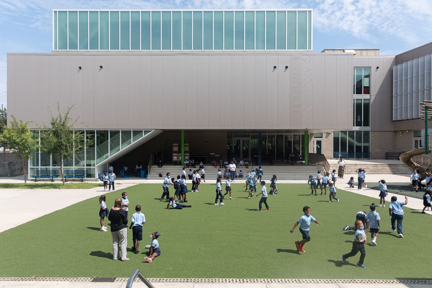 Modern school building exterior with children playing on artificial turf playground.