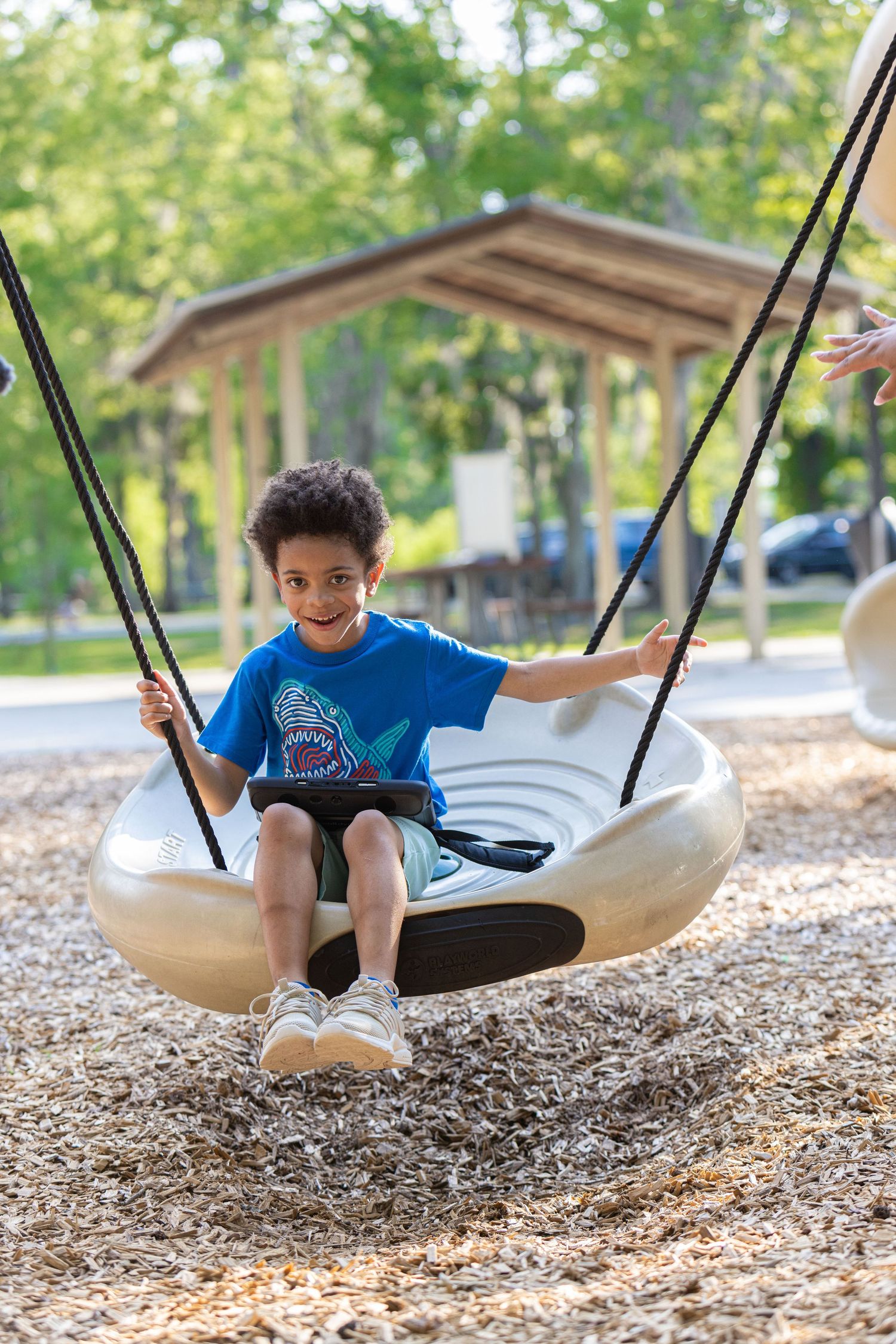 Young child in blue t-shirt smiling while swinging on a modern disc swing at a playground.