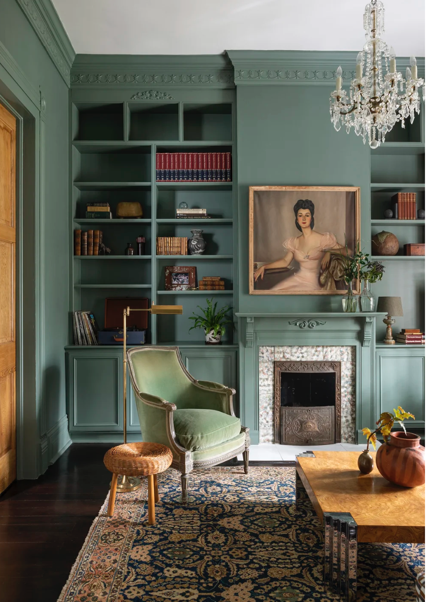 Elegant living room with sage green built-in shelving, crystal chandelier, vintage furniture and Persian rug.