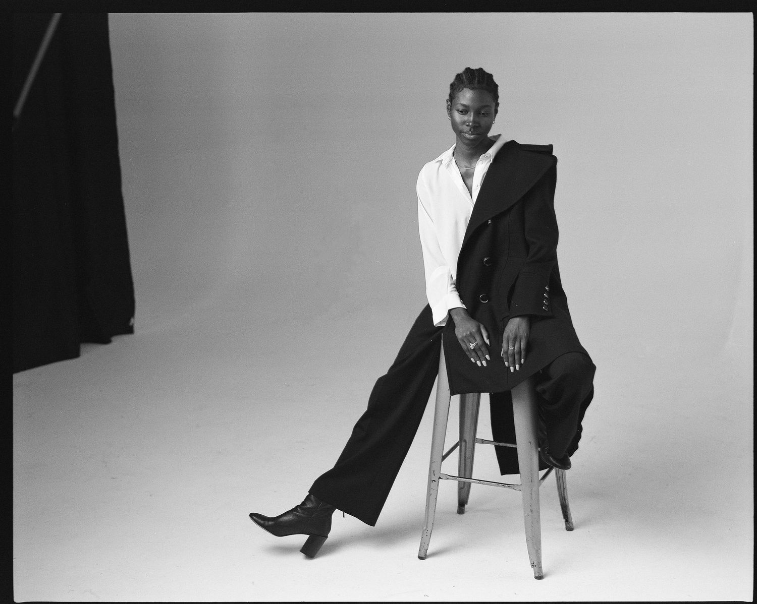 Artistic black and white portrait of a figure seated on a stool wearing white shirt and dark pants.