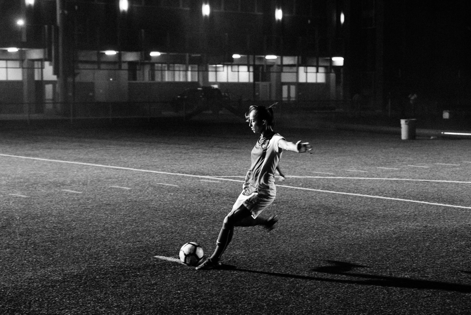 Soccer player kicking ball on illuminated field at night in dramatic black and white composition.