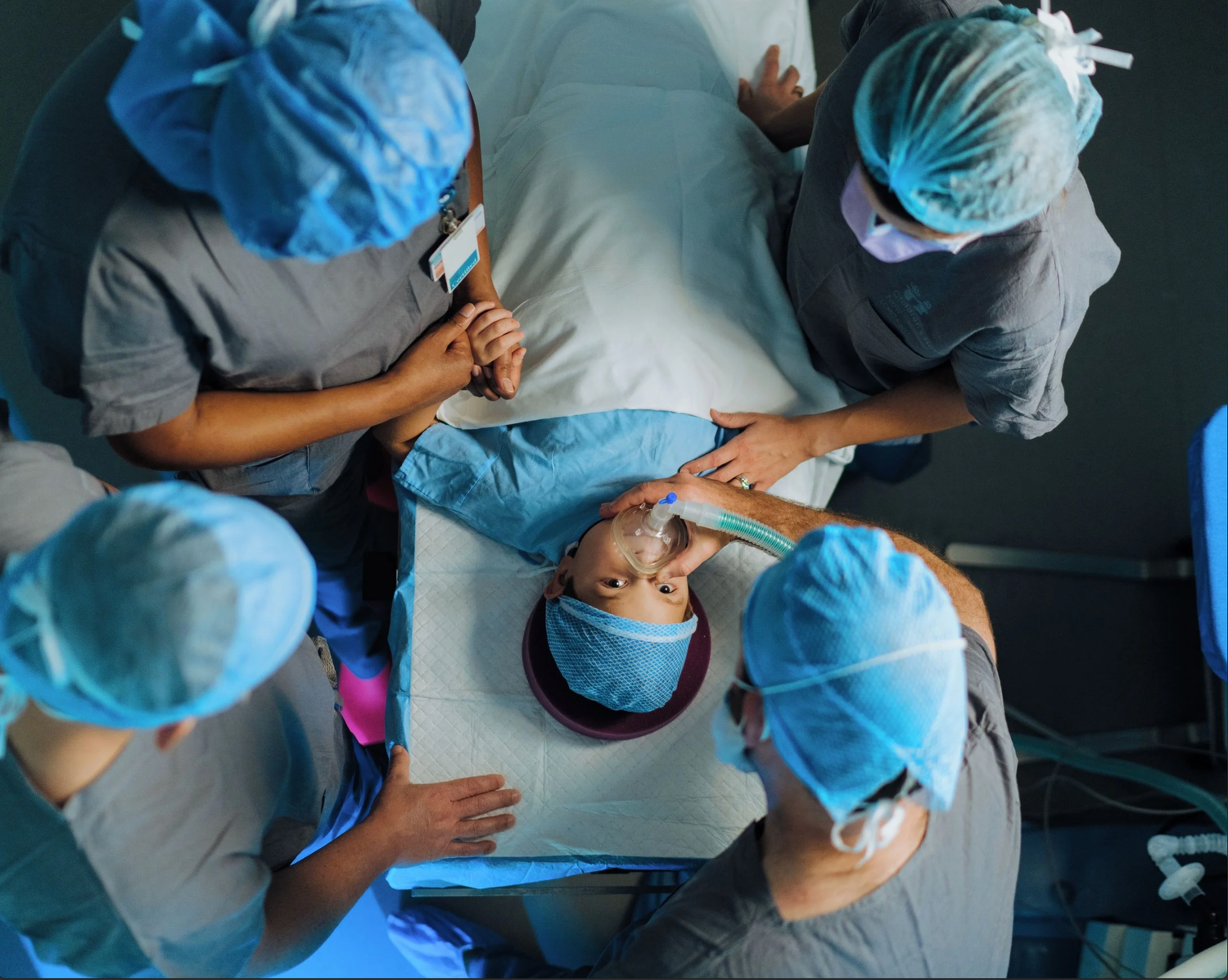 Medical professionals in blue scrubs and surgical caps perform a surgical procedure in an operating room.