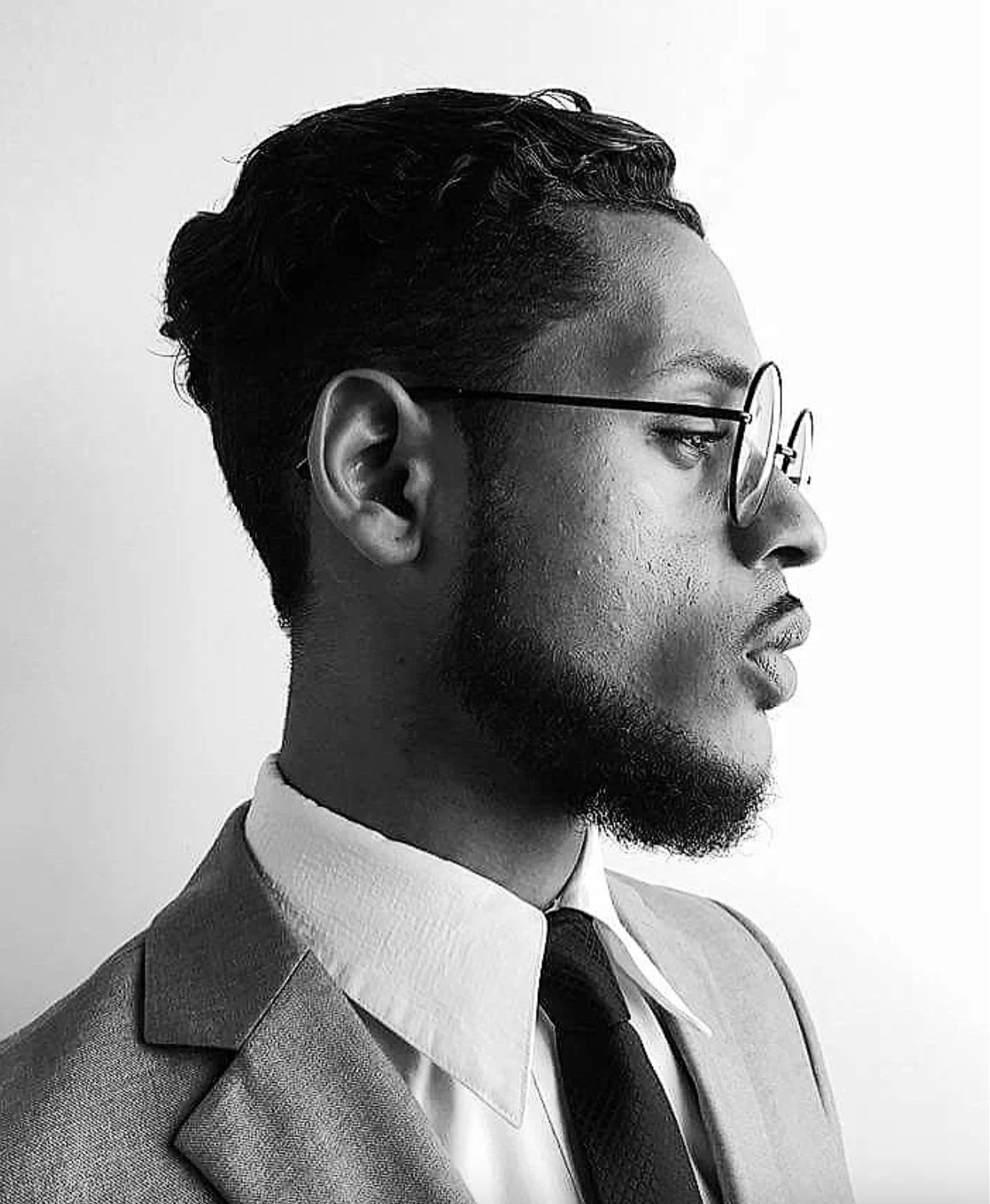 Professional black and white portrait of a person in glasses and suit looking to the side.