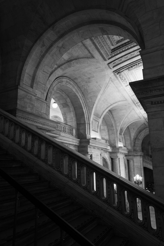 Diagonal view of arched stone corridors with dramatic lighting creating shadows in historic architecture.