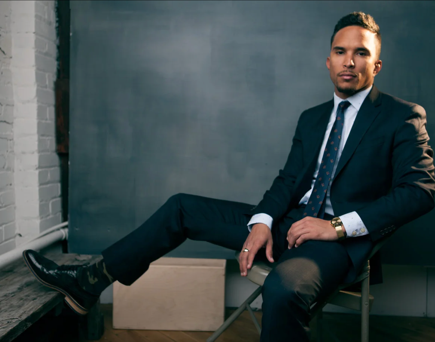 Moody studio portrait of a person in a dark suit against a grey background.