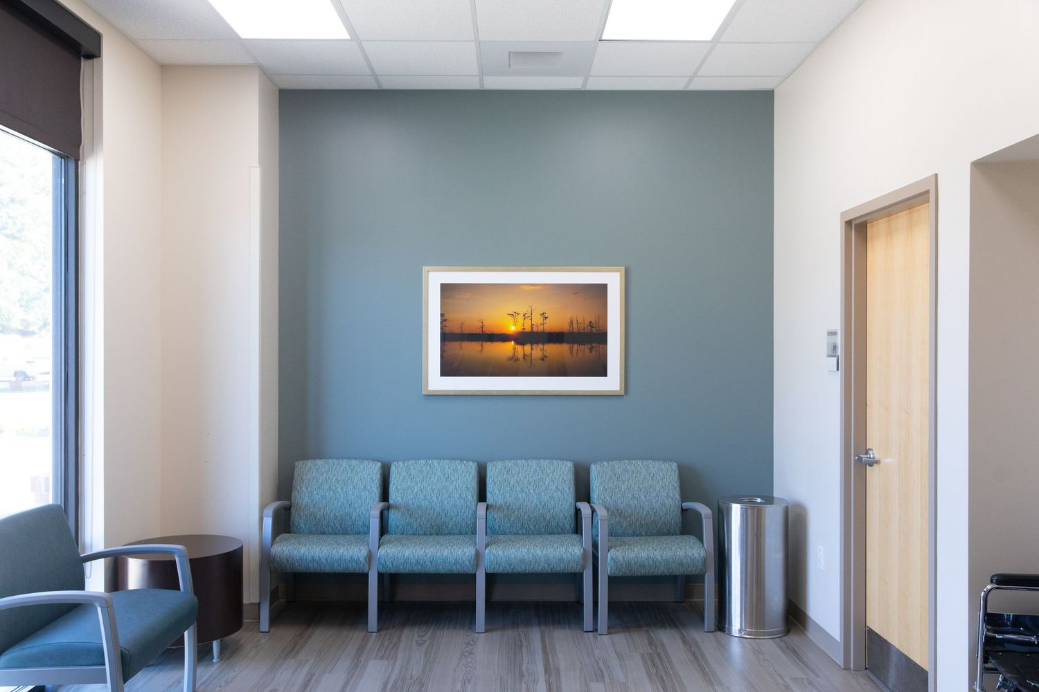 Medical waiting room with blue accent wall and coastal sunset artwork.