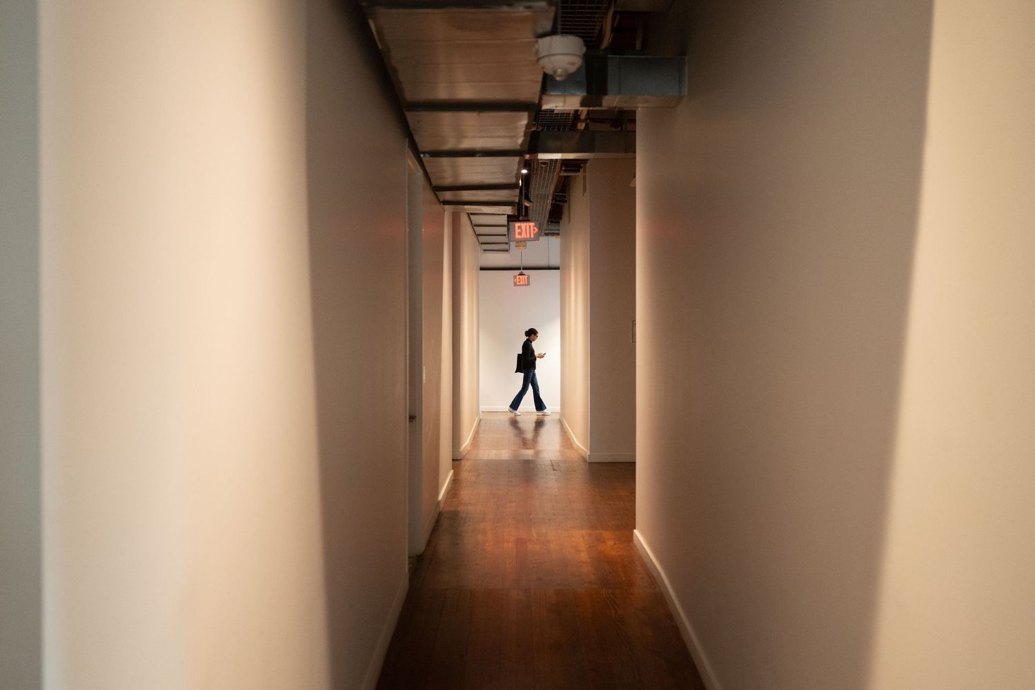 Long empty corridor with dramatic lighting and silhouetted figure walking in the distance.