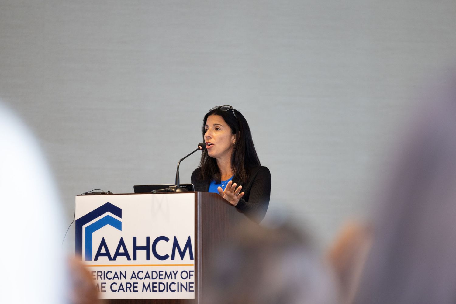 A presenter speaks at a podium with the AAHCM medical conference logo.
