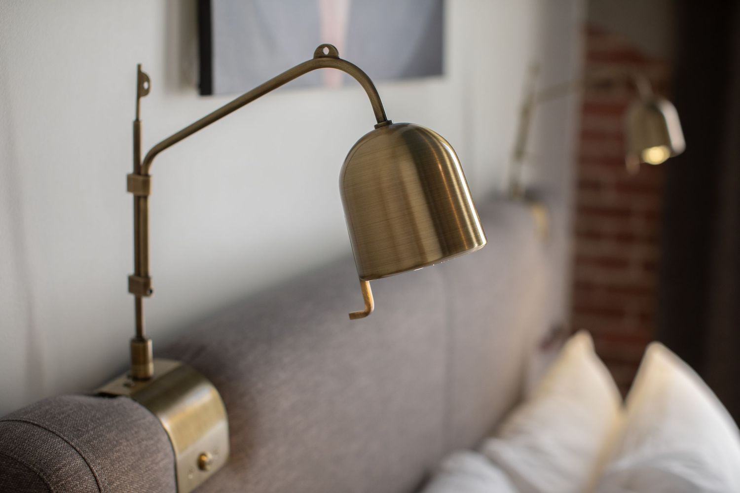 Vintage brass adjustable wall lamp mounted next to a gray upholstered headboard.
