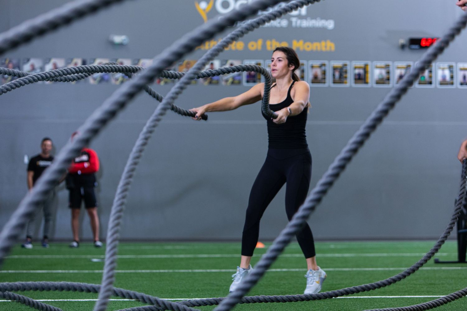 Person exercising with battle ropes in an indoor sports facility.