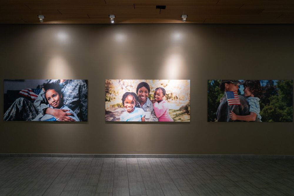 Three large illuminated photographs displayed on a gallery wall with spotlights.