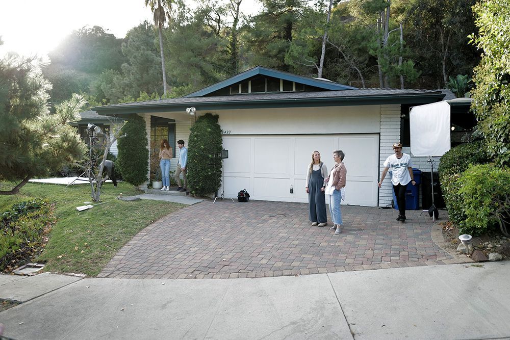People standing on a brick driveway outside a mid-century modern home with a two-car garage and lush green trees.