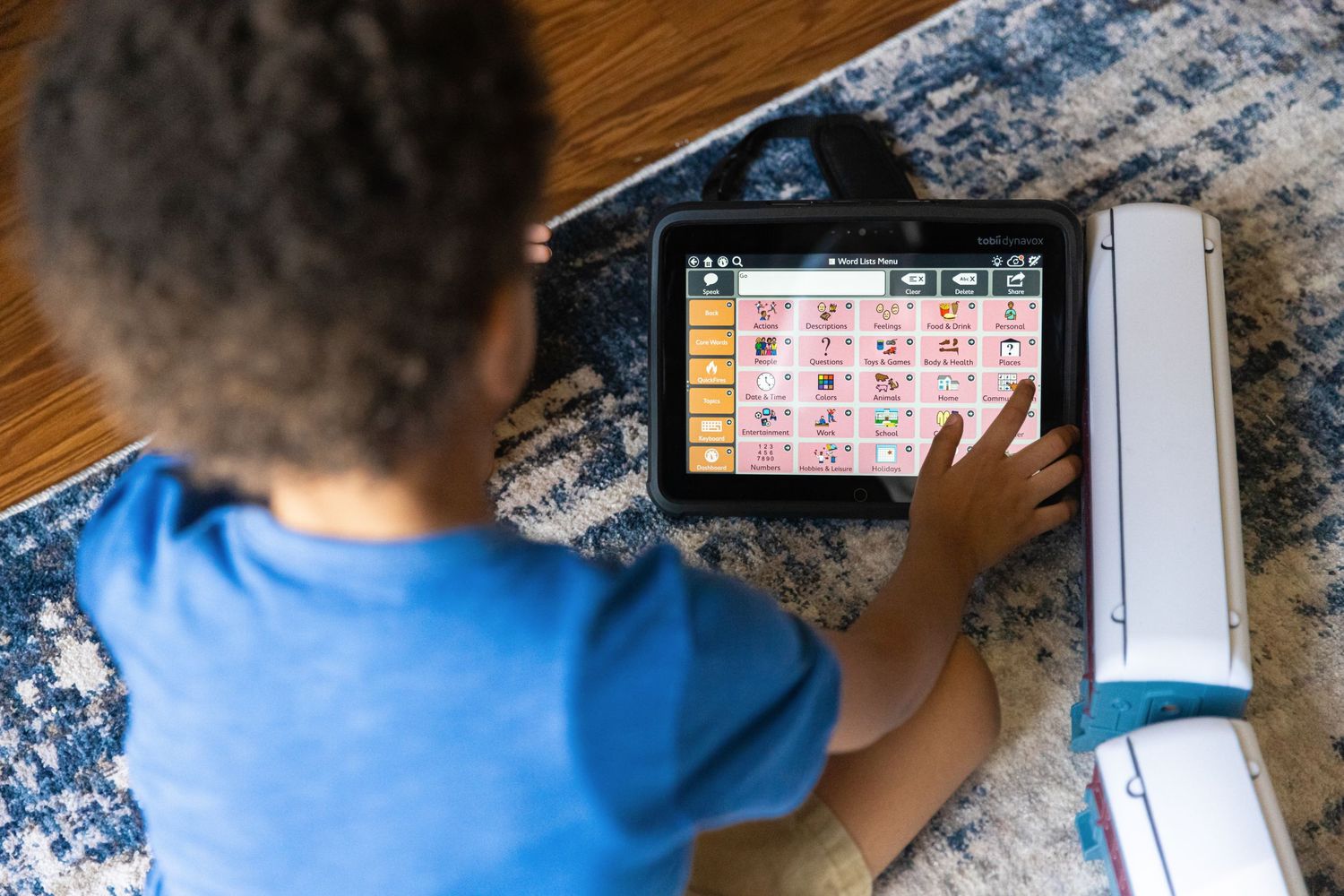 Child using educational tablet device while sitting on patterned blue rug.