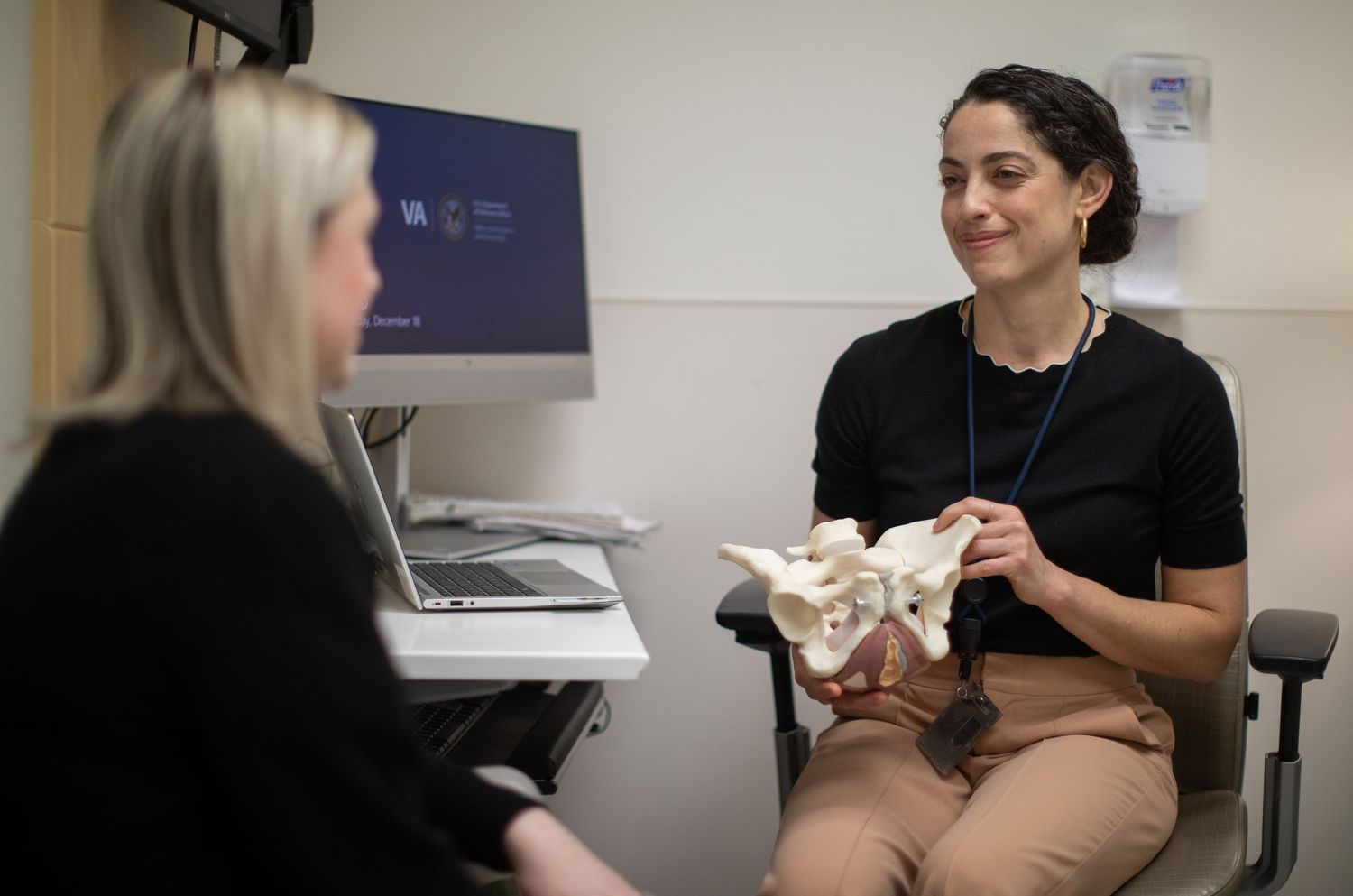 Medical professional discussing anatomical model with colleague in consultation room.