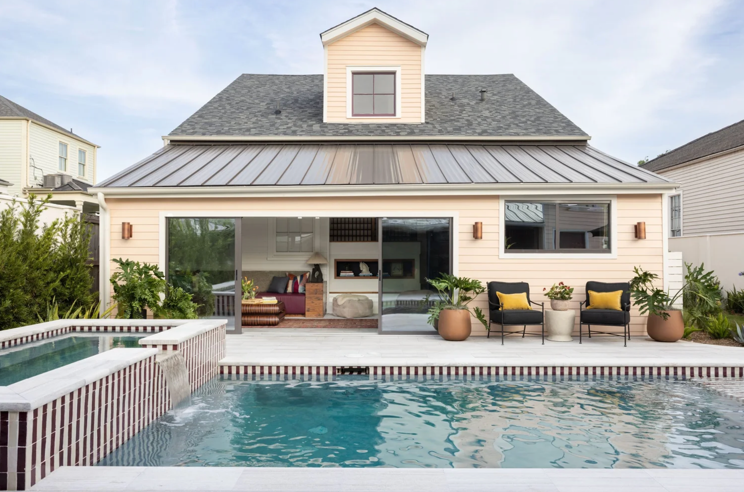 A modern swimming pool with a white fence and covered patio area featuring comfortable lounge seating.
