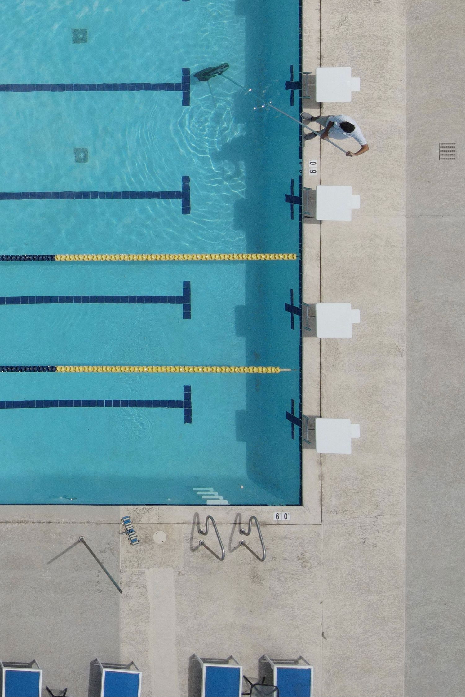 Aerial view of swimming pool lanes with white starting blocks and blue lounge chairs.
