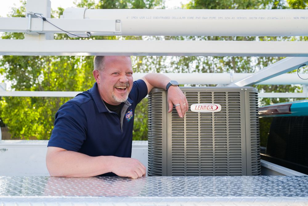 HVAC technician in navy polo shirt smiling beside a Lennox air conditioning unit on a rooftop installation.