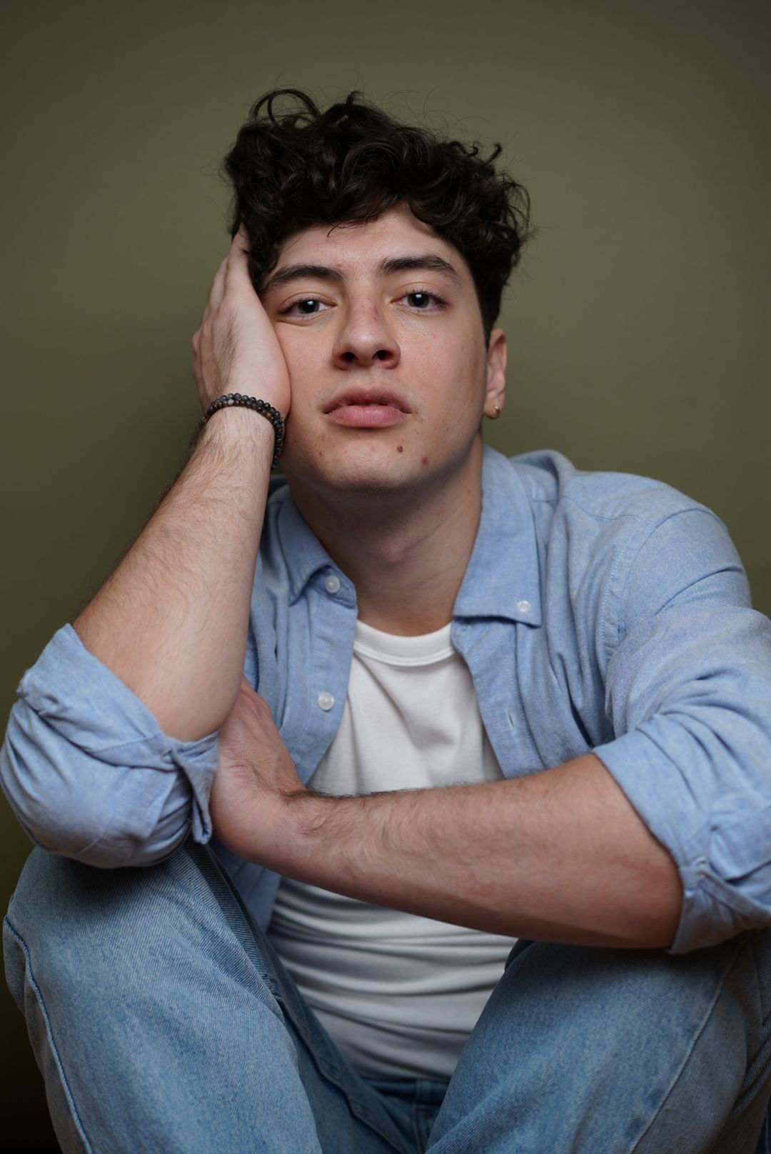 A person in a light blue denim shirt and white t-shirt poses against a dark green background in various positions.