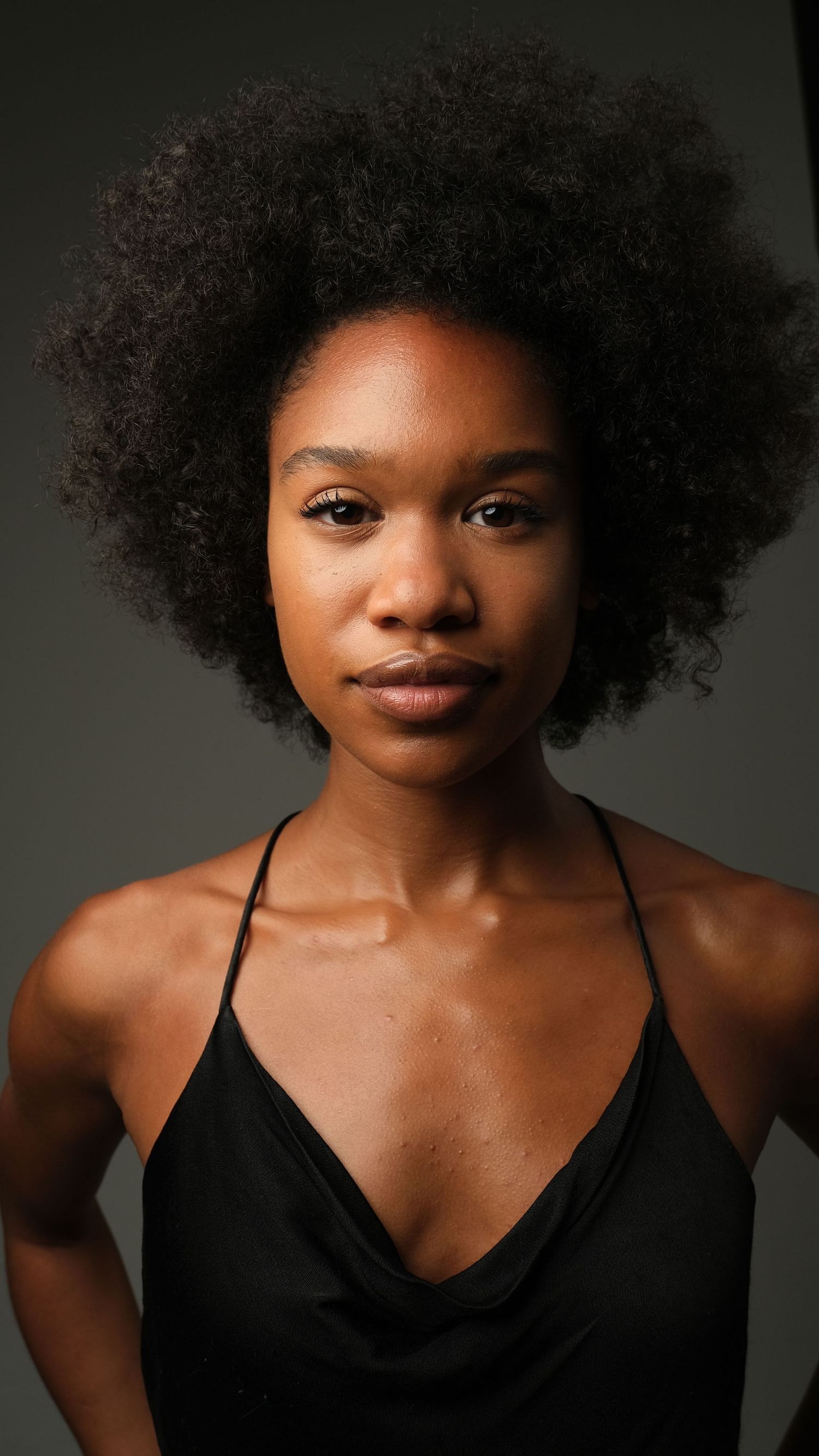 Studio portrait with natural afro hairstyle wearing a black tank top against dark background.
