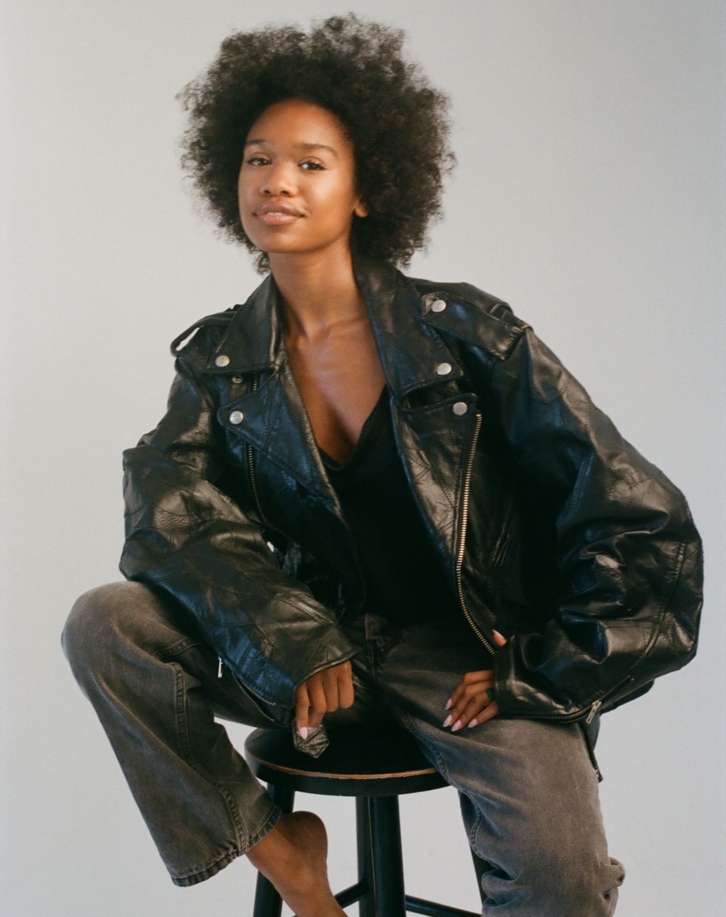 Figure in a black leather jacket and curly hair poses in various fashion shots against a gray background.