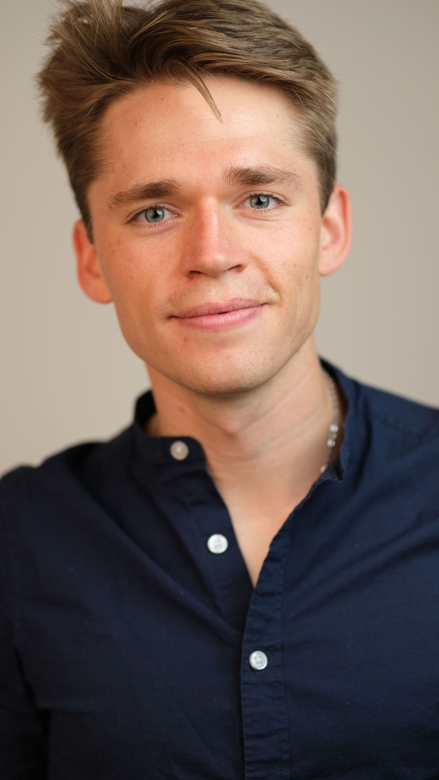 Professional headshot of a young person wearing a navy blue button-down shirt against a neutral background.