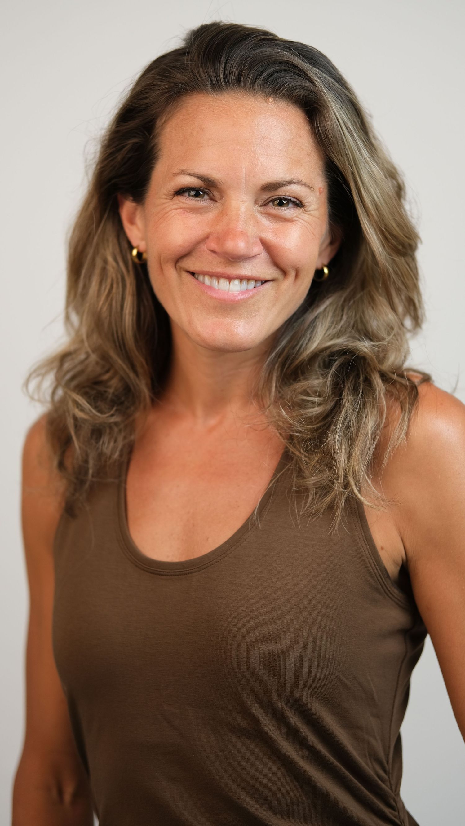 Natural studio portrait wearing brown tank top with wavy hair.