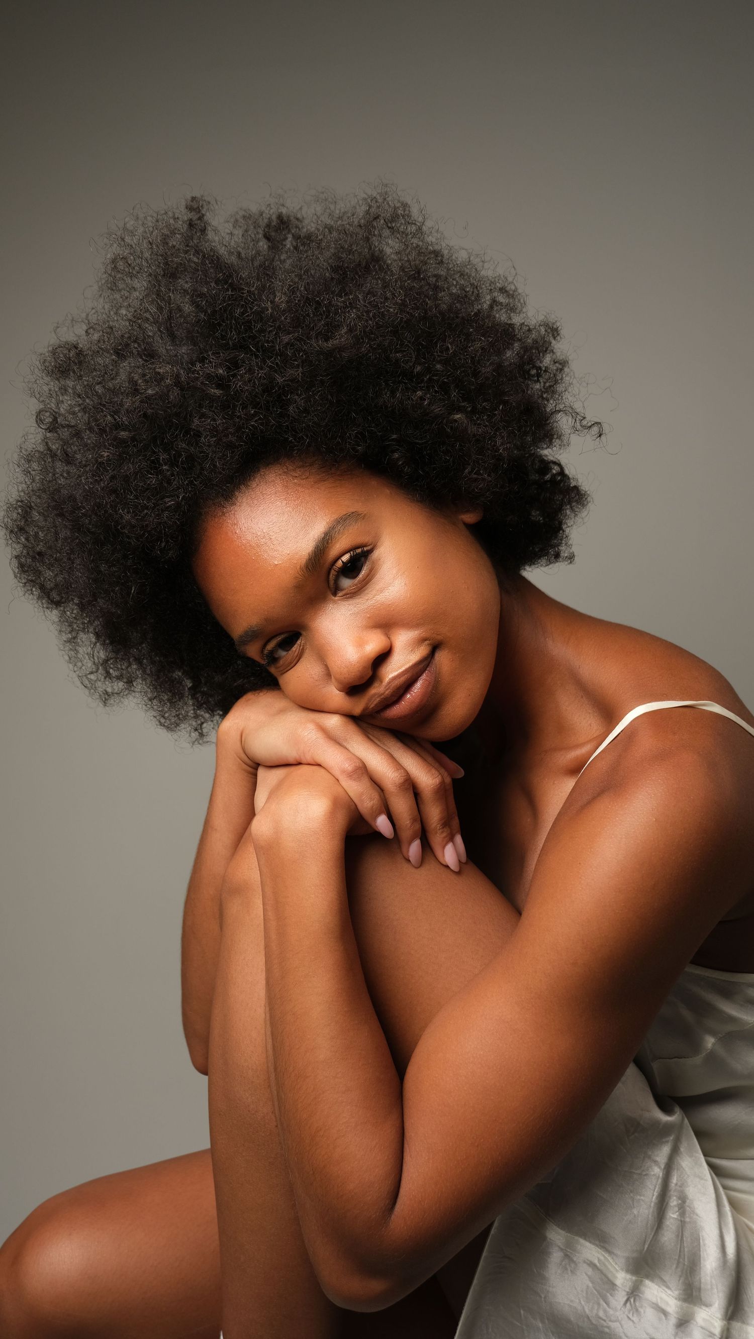 Elegant portrait featuring natural afro hairstyle and white fabric against grey background.