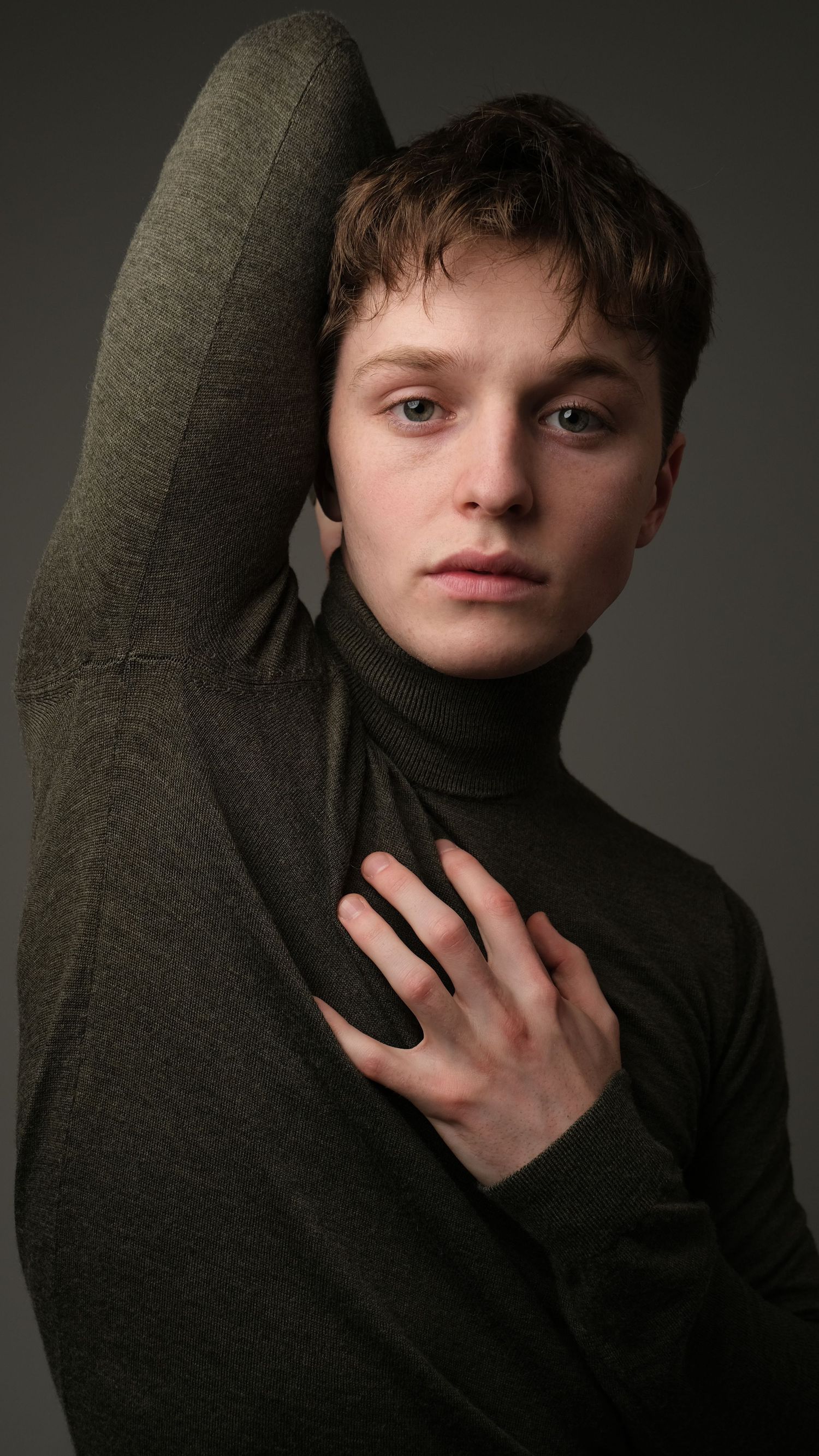 Artistic portrait featuring someone in dark turtleneck sweater with moody studio lighting.