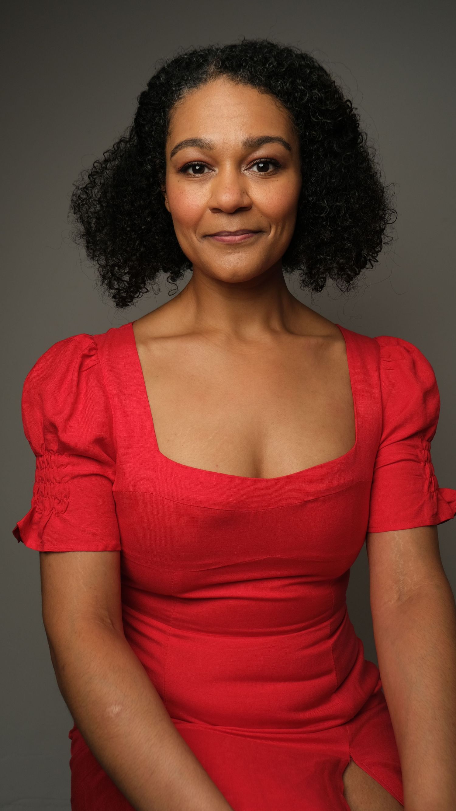 Portrait session featuring a woman in a red dress with puff sleeves against a neutral background.