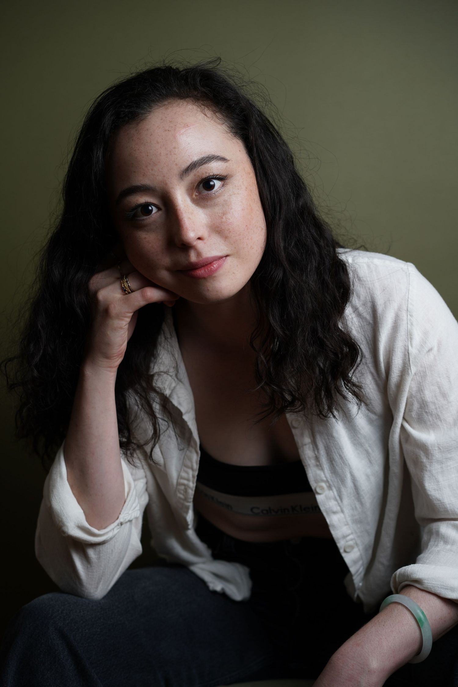 A series of artistic portrait shots showing someone in a white shirt against a dark background leaning on their hand.