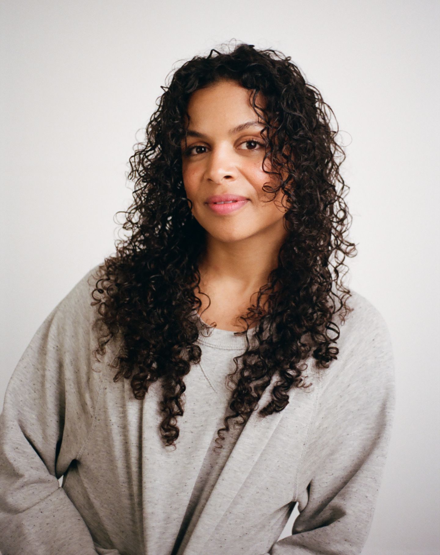 A four-panel sequence showing a person with curly dark hair in a grey sweatshirt posing against a white background.