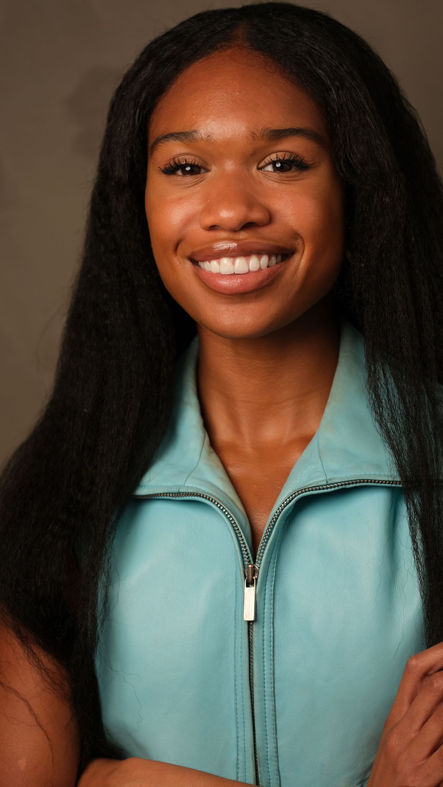 Professional headshot of someone wearing a turquoise zip-up top and long black hair against a neutral background.